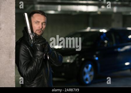 Junger Mörder oder Agent in schwarzer Lederjacke und Handschuhen mit Handfeuerwaffe Stockfoto