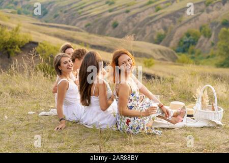 Die Firma fröhliche weibliche Freunde in weißen Kleidern mit Blick auf die grünen Hügel, entspannen Sie bei einem Picknick Stockfoto