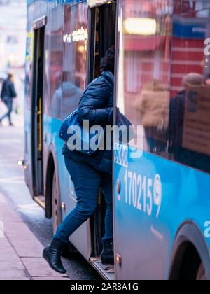 Moskau, Russland - 17. Januar 2020: Der blaue M27-Bus fährt zu einer Haltestelle des öffentlichen Verkehrs. Stadtstraße mit Bussen. Frau betritt die Tür Stockfoto