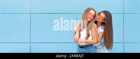 Zwei junge Hipster Frau Freunde in retro neon Sonnenbrille stehen und Lächeln über blaue Wand Stockfoto