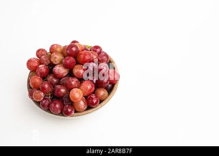 Ein Haufen frischer roter Trauben, die auf einer kleinen Keramikschale auf einem einfarbigen weißen Hintergrund gebündelt sind. Stockfoto