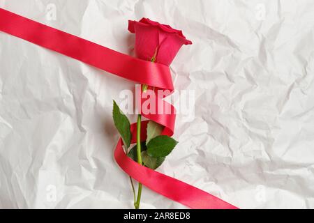 Schöne rote Rose mit Band auf zerknittertem Papier. Draufsicht. Stockfoto