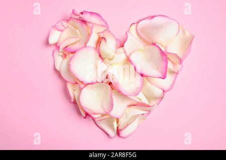 Ein wunderschönes Herz aus weißen und rosafarbenen Rosenblättern auf einem Papierhintergrund. Draufsicht. Stockfoto