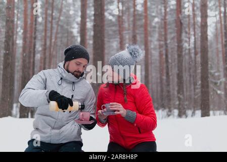 Junge Paare haben Picknick im winterlichen verschneiten Wald, Mann gießt Tee Stockfoto