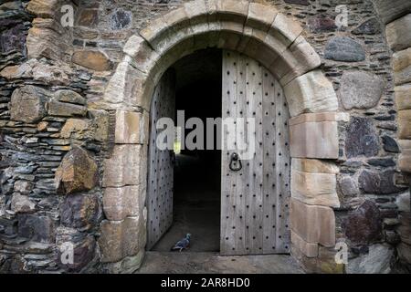 Die Tordurchfahrt hat eine massive, abgenutzte Holztür, die von Steinziegeln umgeben ist. Dunstaffnage Castle aus dem 13. Jahrhundert ist eine der ältesten Burgen Stockfoto