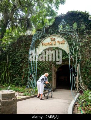 Die kacuasische Frau im hohen Alter lehnt sich an einen Wanderer, um den mit Weinstock bedeckten Eingang zum Jungbrunnen in St. Augustine, Florida, USA, zu betreten Stockfoto