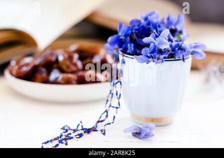 Schüssel mit süßlich leckeren getrockneten Datumsfrüchten in einer Komposition mit violetten Blumen und Vintage-Büchern. Ramadan, traditionelle Küche. Stockfoto