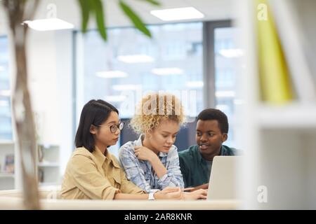 Porträt der multiethnischen Gruppe von Studenten, die Laptop zusammen verwenden, während sie an Projekten in der Bibliothek arbeiten, Kopierraum Stockfoto