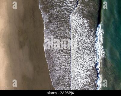 Wellen waschen sich an einem sandigen Strand. Blick von oben nach unten. Stockfoto