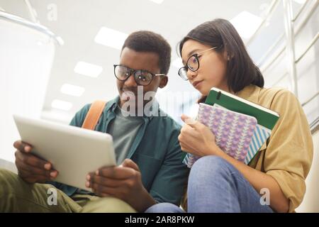 Porträt zweier internationaler Studenten, die gemeinsam Bücher lesen, während sie an Projekten in der modernen Hochschulbibliothek arbeiten Stockfoto