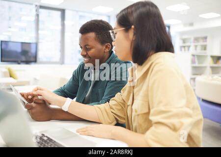 Porträt von zwei Studenten, die in der Hochschulbibliothek studieren, Schwerpunkt auf asiatische junge Frau, die Laptop im Vordergrund verwendet Stockfoto