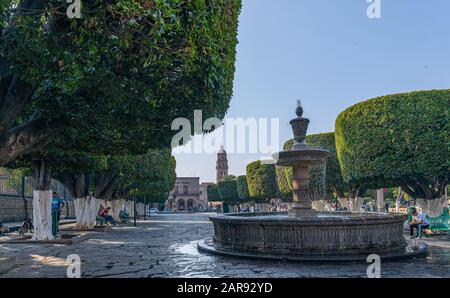 Morelia, Michoacan, Mexiko - 24. November 2019: Brunnen an der Plaza de Armas und der San Agustin Tempel im Hintergrund Stockfoto