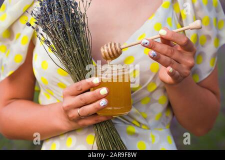 Ein Mädchen im Kleid steht inmitten eines Lavendelfeldes. In ihren Händen ist ein Blumenstrauß aus Lavendel und ein Glas Honig. Valensole, Provinz Frankreich Stockfoto