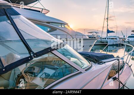 Cockpit und Steuerpult eines kleinen Marineboots im Hafen. Yachts am Pier. Schöner klarer Sonnenuntergang im Meereshafen mit Segelyachten. Stockfoto