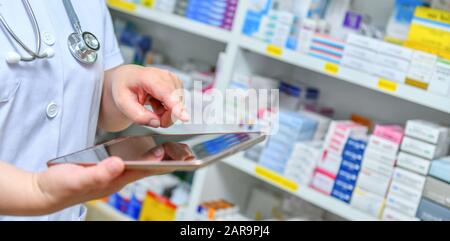 Arzt verwendet Computertablette für Suchleiste auf Anzeige in Apotheken-Drogerie-Regalen Hintergrund.Online medizinisches Konzept. Stockfoto