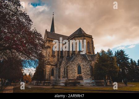 BARILOCHE, ARGENTINIEN, 18. JUNI 2019: Farbenfroher Pfad mit roten Bäumen neben der Kathedrale Nuestra Senora del Nahuel Huapi. Stockfoto