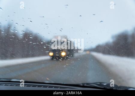 Verschwommener Blick durch die Windschutzscheibe in den Regentropfen auf der Autobahn, die sich in Richtung eines großen Autos bewegt. Selektiver Fokus Stockfoto