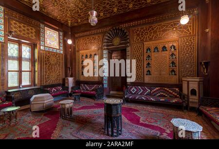 Der Palast von Prinz Mohammed Ali. Gästesaal mit verzierter Holzdecke, verzierter Holztür, Laternen, farbenfrohen, verzierten Sofas, Teetischen und verzierten Teppichen, Kairo, Ägypten Stockfoto