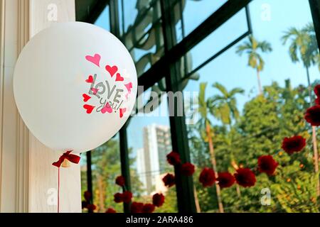Der weiße Ballon mit rosafarbenen Herzen und die Worte LIEBEN dich! Schwebend am Fenster des Raums Stockfoto