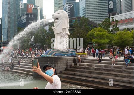 26.01.2020, Singapur, Republik Singapur, Asien - EINE junge Frau bedeckt ihr Gesicht mit einer chirurgischen Maske und nimmt ein selfie im Merlion Park. Stockfoto