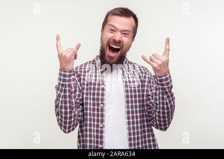 Porträt eines verrückten freudigen bärtigen Mannes in Plaid Hemd mit Rock- und Roll-Zeichen-Handgeste und schreien mit Spannung, Gefühl, cooler Rocker zu sein. Stockfoto