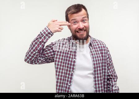 Tötet mich. Porträt eines verrückten, müden bärtigen Mannes in einem lässigen Kraghemd, das mit der Fingerpistole auf den Kopf zeigt, Selbstmord begeht, depressiv erschöpft aussieht, aber mA Stockfoto