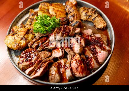 Frische, saftige Sortiment von geschnittenen Fleisch vom Grill, die auf eine große und runde Platte liegt, mit Petersilie auf der Oberseite dekoriert. Stockfoto