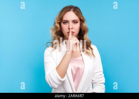 Sei still! Porträt der unzufriedenen wütenden Dame mit gewelltem Haar in weißer Jacke, die mit dem Finger auf den Lippen ein Hush-Zeichen macht, Stille und Geheimhaltung fordert, halten Sie c Stockfoto