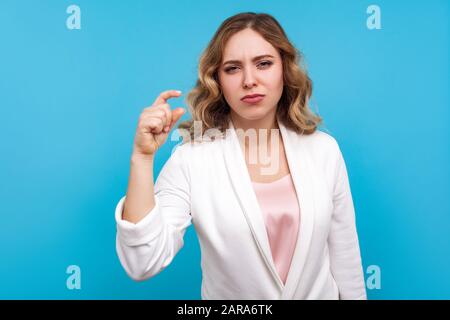 Noch etwas, bitte. Porträt einer unzufriedenen Frau mit gewelltem Haar in weißer Jacke, die ein wenig Geste und ein wenig Stirnrunzle macht und kleine Größe misst. IND Stockfoto