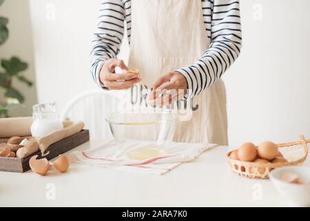 Männliche Hände brechen ein Ei in die Schüssel Teig auf weißen Tisch zu machen Stockfoto