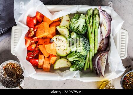 Kochen von Gemüse zum Backen in der Ofenform. Roher Pfeffer, Süßkartoffel, Spargel, Brokkoli und Zwiebeln mit Öl und Gewürzen. Stockfoto