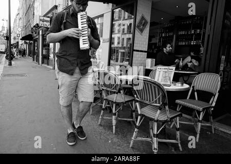 Mann, der auf der Tastatur Mundharmonika, Mundorgel, Café auf dem Straßenbelag, Rue Saint Antoine, Paris, Frankreich, Europa spielt Stockfoto