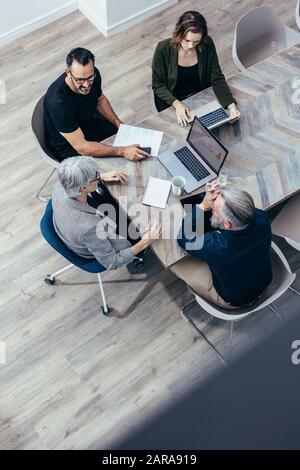 Draufsicht über das Business-Team, das um einen Tisch sitzt und diskutiert. Eine hochwinkelige Ansicht von Geschäftsleuten, die eine Brainstorming-Sitzung haben. Stockfoto