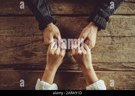 Direkt über dem Schuss eines Paares, das um den Tisch sitzt und die Hände hält. Nahaufnahme von Mann und Frau in Liebe, die Hände über einen Holztisch halten. Stockfoto