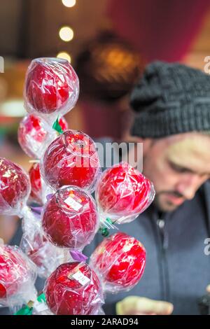 Umhüllte Toffee Äpfel, die mit einem männlichen Kunden im Hintergrund auf dem Weihnachtsmarkt im Winterwunderland von London ausgestellt werden Stockfoto