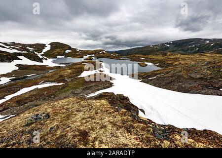 Typisch norwegische Landschaft mit schneebedeckten Bergen und Clear Lake in der Nähe der berühmten Aurlandsvegen (Bjorgavegen), Mountain Road, Aurland, Norwegen. Stockfoto