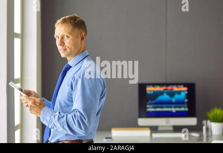 Portrait von lächelnden glückliche junge Unternehmer stehen in seinem Büro Tisch und Arbeiten auf Tablet-PC Stockfoto