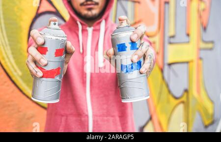 Junger Mann mit zwei lächelnden Sprays - Graffiti-Künstler-Gemälde mit Aerosolfarbdosen an der Wand - urbaner Lebensstil, Jugend, tausendjähriges Generat Stockfoto