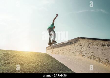 Junger Mann, der mit Skateboard auf der Rampe bei Sonnenuntergang im städtischen Park auftrat - Skater, der mit Rückensonnenlicht Spaß hat - Extremsport, tausendjährige Generatio Stockfoto