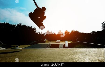 Silhouette junger Skater, die auf der Rampe im Stadtpark springen - Junge, der Tricks und Fähigkeiten mit Skateboard bei Sonnenuntergang ausführt - Jugend-Lifestyle und extremer sp Stockfoto