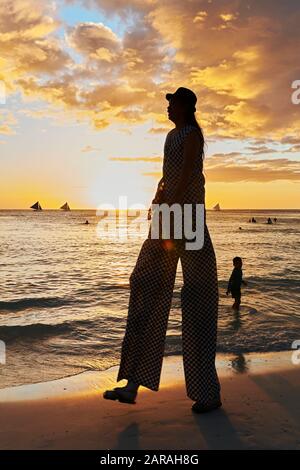 Boracay, Aklan, Philippinen - 1. Januar 2020: Jongleur auf Stelzen, die bei Sonnenuntergang am weißen Strand spazieren gehen, mit einem kleinen Jungen, der ihn beobachtet Stockfoto