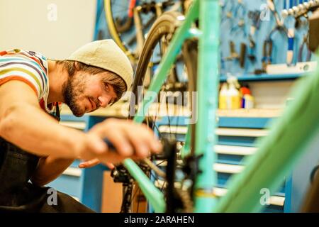 Stilvoller bärtiger Fahrradmechaniker, der seine Arbeit in der Werkstatt macht - Junger trendiger Mann, der neue Carbonfaser-Superbike-Halle überprüft - Repairing Bik Stockfoto