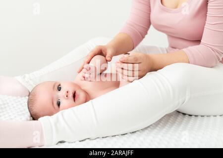 Hintergrund der Babymassage. Mutter massiert ihren kleinen Jungen sanft. Baby, das auf dem Rücken liegt und während der Massage auf die Kamera blickt. Stockfoto
