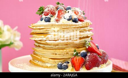 Shrove Pancake Dienstag, letzter Tag vor der Fastenzeit, Pfannkuchenstapel, zubereitet mit Schichten von Schlagsahne und frischen Beeren gegen den modernen rosafarbenen Backg Stockfoto