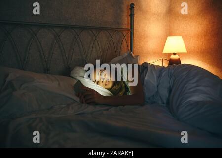 Mädchen benutzt ein Handy, während sie im Bett liegen und lächeln. Stockfoto
