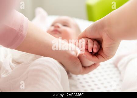 Die Mutter massiert ihren kleinen Jungen sanft, während sie ihm Körperlotion auf die Haut aufgetragen hat. Hintergrund der Babymassage. Hände nah an. Stockfoto