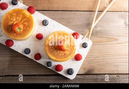 Hausgemachte japanische Hotcakes auf Holzhintergrund mit Himbeeren, Brombeeren und Erdbeeren und Zuckerpulver. Top View. Stockfoto