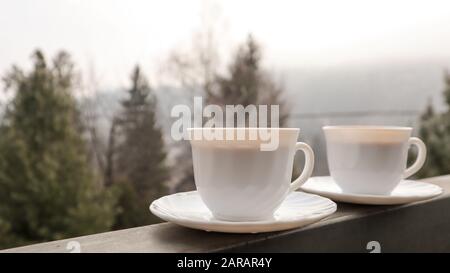 Zwei Kaffeetassen auf einem Balkon mit Berglandschaft am Morgen. Zwei Tassen Morgenkaffee, seitlich auf dem Balkon stehend, mit einem zauberhaften Stockfoto