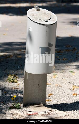 Abfalleimer aus grauem Metall mit geschlossenem Oberteil auf Betonfundament, umgeben mit kleinkörnigem Kies im öffentlichen Park Stockfoto