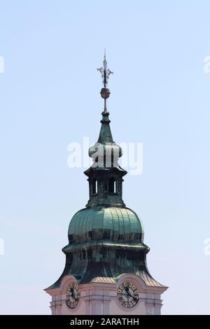 Alter Kirchturm aus Kirche mit allseits analogen Uhren und großem Metallkreuz oben bedeckt mit grünen Metallfliesen auf hellblauem Himmelshintergrund Stockfoto